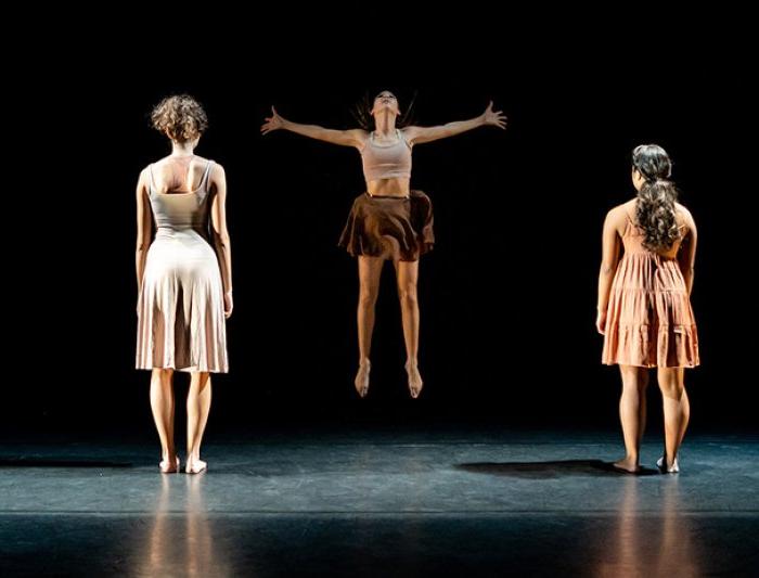 A group of dancers with their backs to the audience while the middle dancer jumps